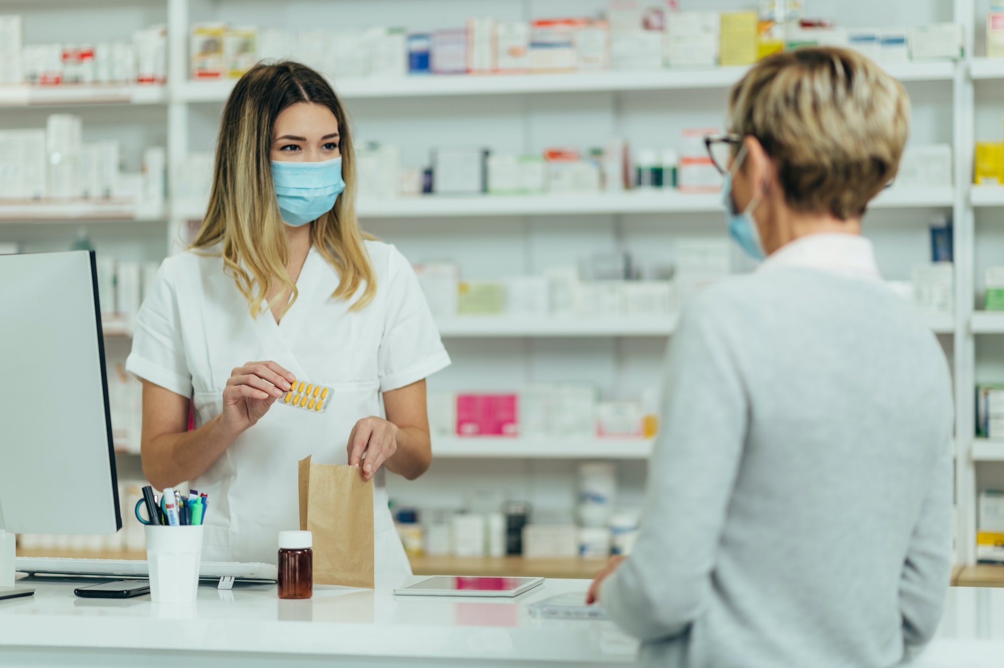 Pharmacist wearing protective mask and serving a customer patient in a pharmacy